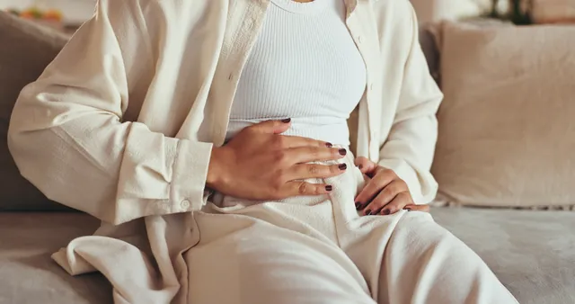 Femme assise sur un canapé, les mains posées sur le bas du ventre