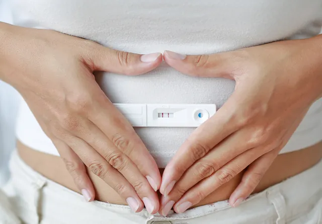 Mains formant un cœur autour du ventre, un test de grossesse posé devant